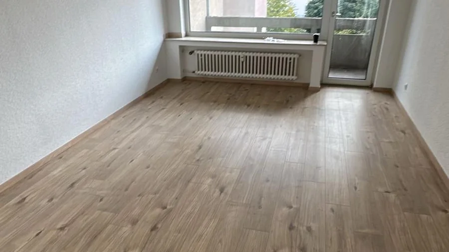 Neu verlegter Boden in Holzoptik in einem leeren Wohnzimmer mit Balkontür
